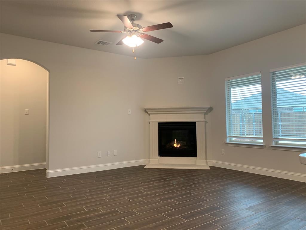765 Knoxbridge Road Forney, TX 75126 - Photo 6 of 22 an empty room with wooden floor a ceiling fan and a fireplace