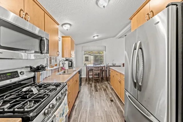 a kitchen with stainless steel appliances granite countertop a stove top oven a sink dishwasher a refrigerator and cabinets with wooden floor