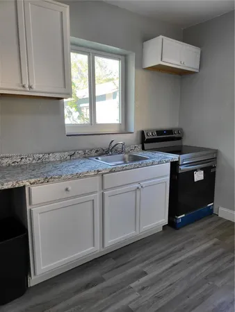 a kitchen with stainless steel appliances granite countertop a stove a sink and white cabinets with wooden floor