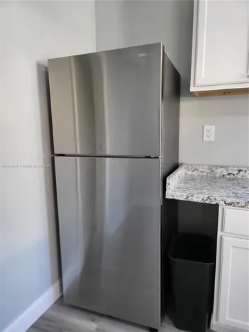 a view of a refrigerator in kitchen and an empty room with wooden floor
