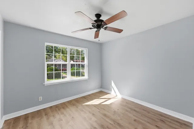 an empty room with wooden floor chandelier and windows