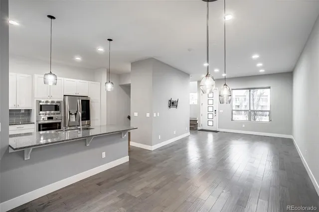 a large kitchen with granite countertop a large kitchen island a sink dishwasher a refrigerator and a wooden floor