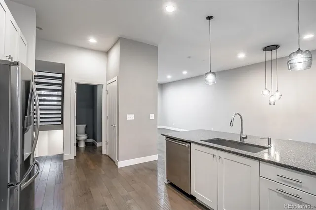 a kitchen with stainless steel appliances granite countertop a sink a refrigerator and a wooden floor