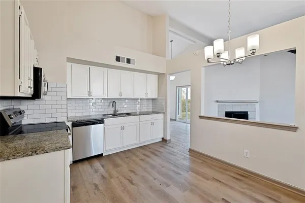 a kitchen with stainless steel appliances granite countertop a refrigerator a sink dishwasher a oven with white cabinets and wooden floor