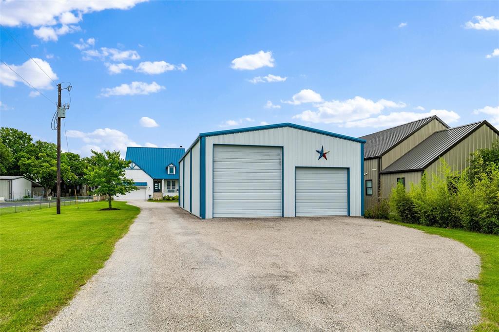 6625 Sandy Beach Road Azle, TX 76020 - Photo 30 of 40 Detached garage features dual overhead garage doors, extended gravel driveway access, vertical siding detail, and surrounding lawn areas positioned separately from the main residence.