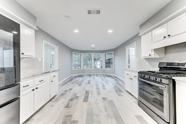 a large kitchen with granite countertop a stove top oven a sink and white cabinets
