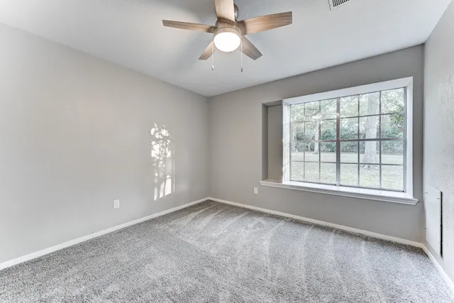 an empty room with chandelier fan and windows