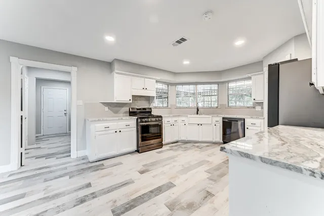 a kitchen with a stove a sink dishwasher a refrigerator and white cabinets with wooden floor