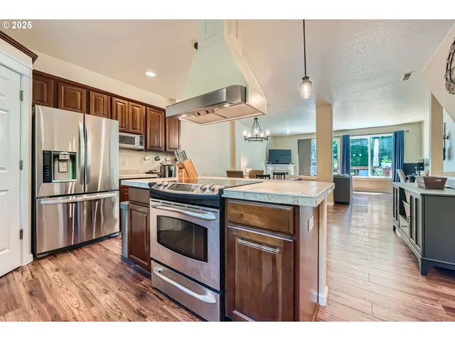 a kitchen with stainless steel appliances kitchen island granite countertop a refrigerator a stove a sink dishwasher a dining table and chairs with wooden floor