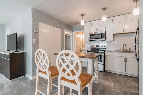 a kitchen with stainless steel appliances a sink a stove a refrigerator cabinets and chairs