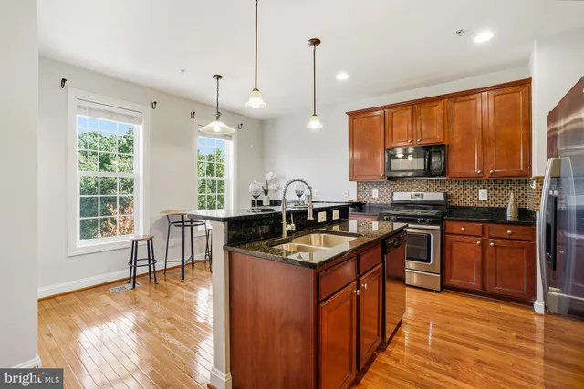 a kitchen with stainless steel appliances granite countertop wooden cabinets a stove a sink a dining table and chairs with wooden floor