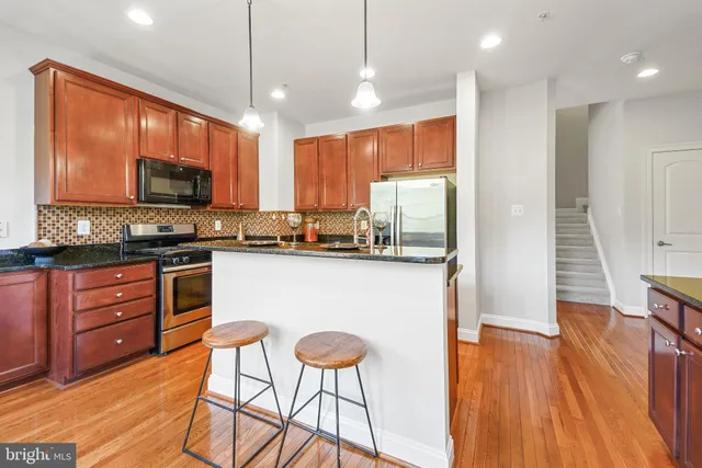 a kitchen with stainless steel appliances granite countertop wooden cabinets a refrigerator a stove a sink and a dining table with wooden floor