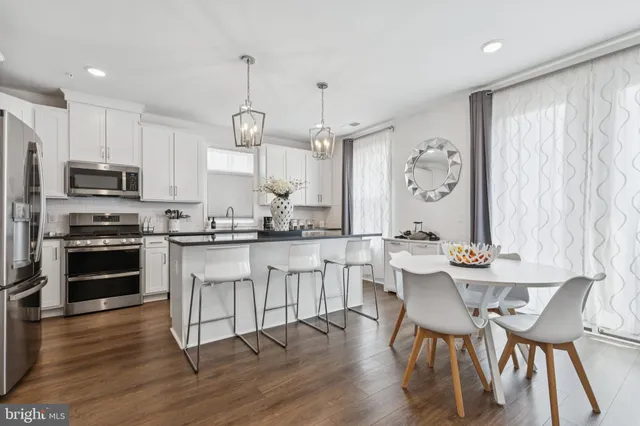 a kitchen with stainless steel appliances kitchen island granite countertop a dining table chairs and a refrigerator