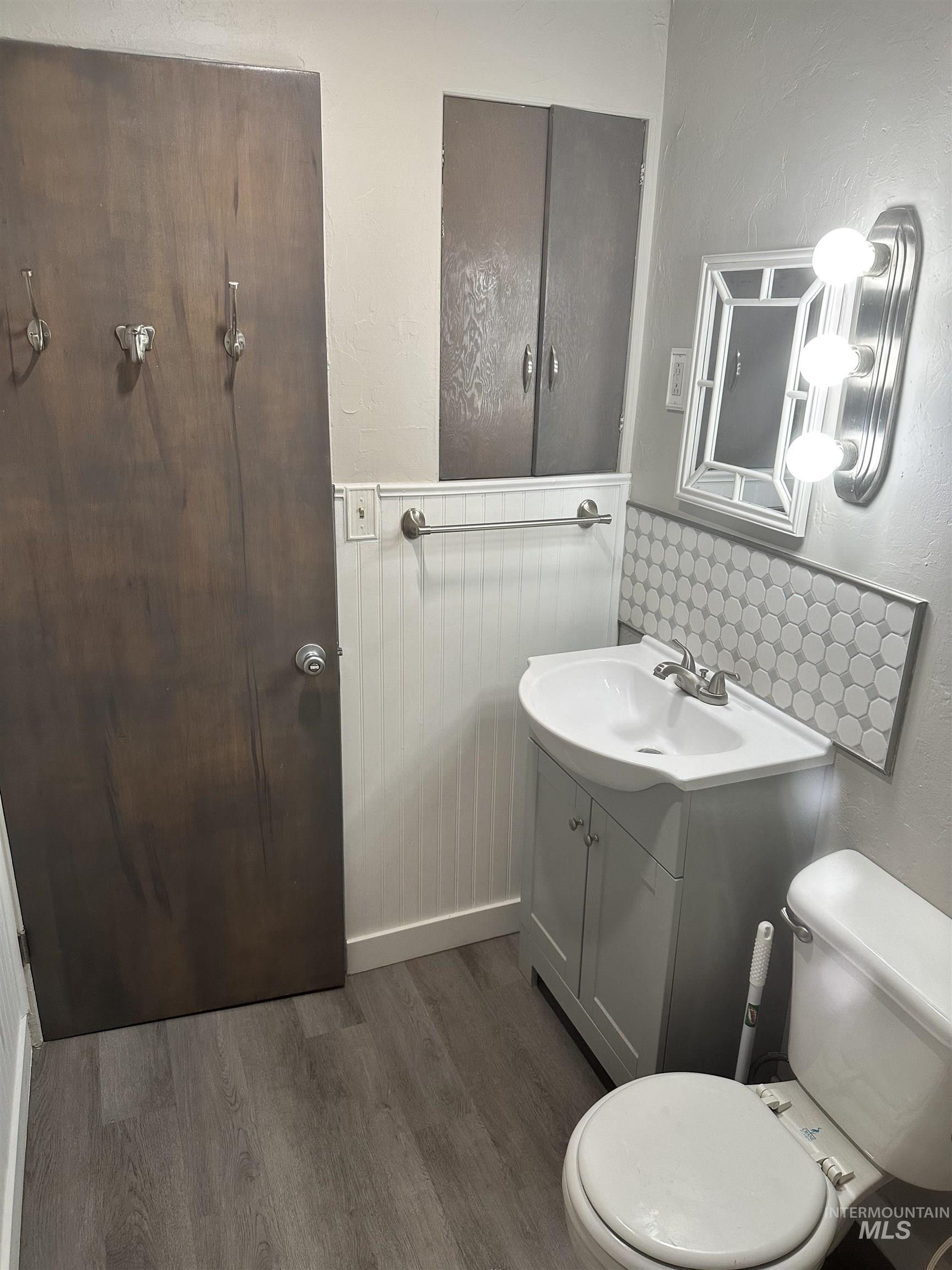 661 Southwest 3rd Street Ontario, OR 97914 - Photo 11 of 45 Bathroom featuring a textured wall, decorative backsplash, vanity, dark wood-type flooring, and a wainscoted wall