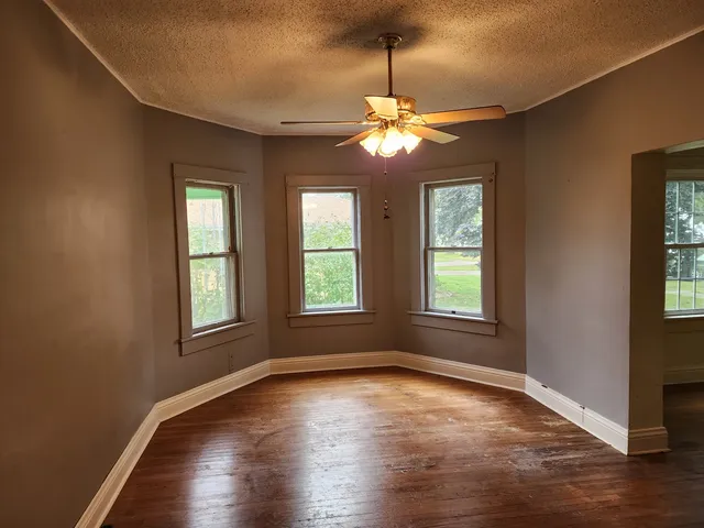 an empty room with wooden floor chandelier and windows