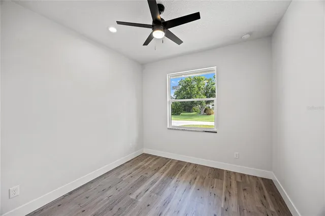 an empty room with wooden floor ceiling fan and window