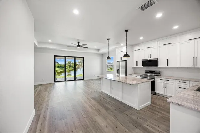 a large kitchen with stainless steel appliances granite countertop a stove top oven a sink dishwasher and a refrigerator with wooden floor