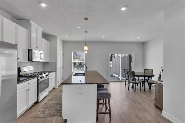 a kitchen with stainless steel appliances granite countertop a stove top oven a sink a dining table and chairs with wooden floor