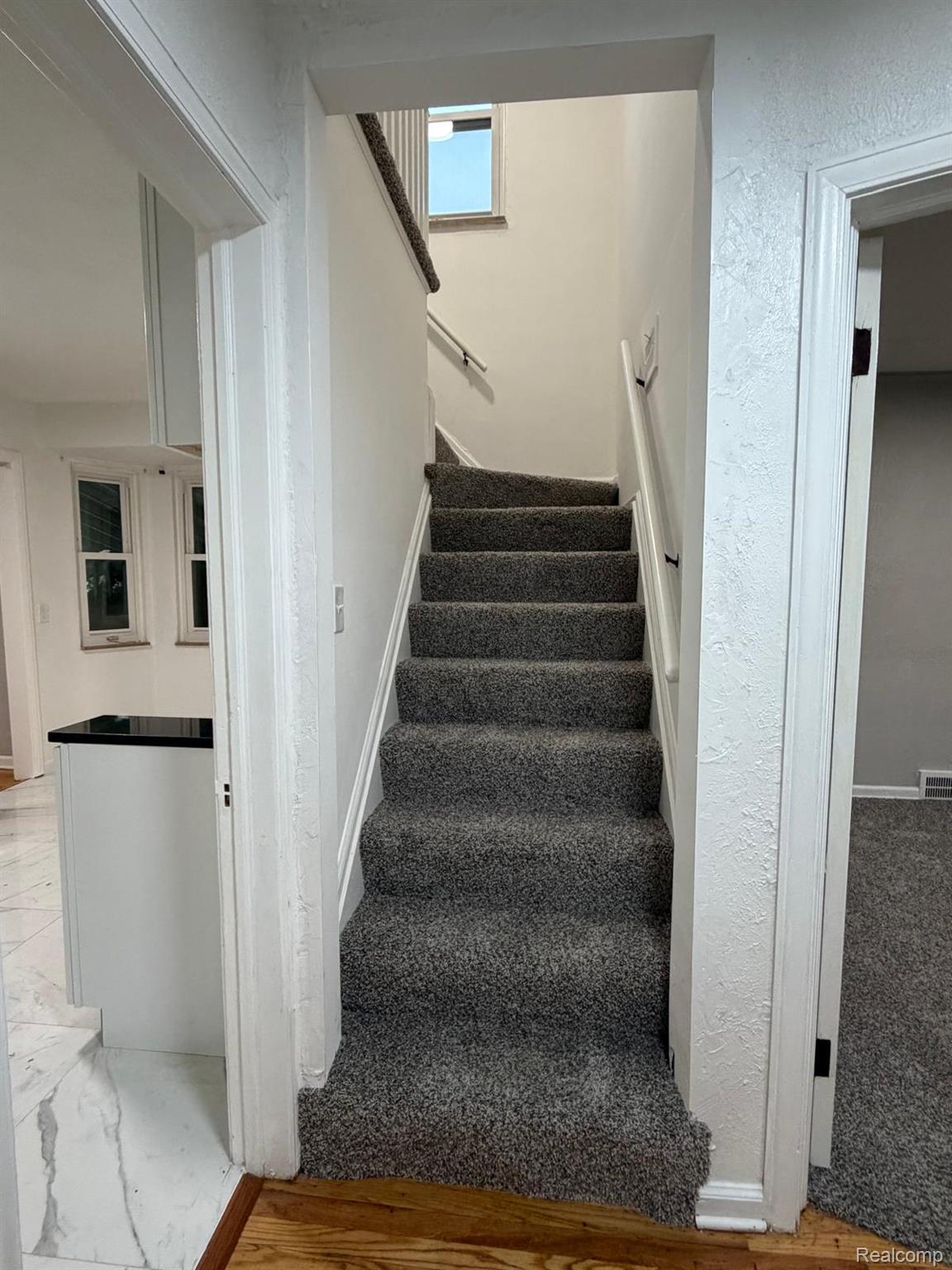 10441 Roxbury Street Detroit, MI 48224 - Photo 15 of 22 Carpeted staircase with white railings, featuring a window on the upper landing, and hardwood flooring at the base