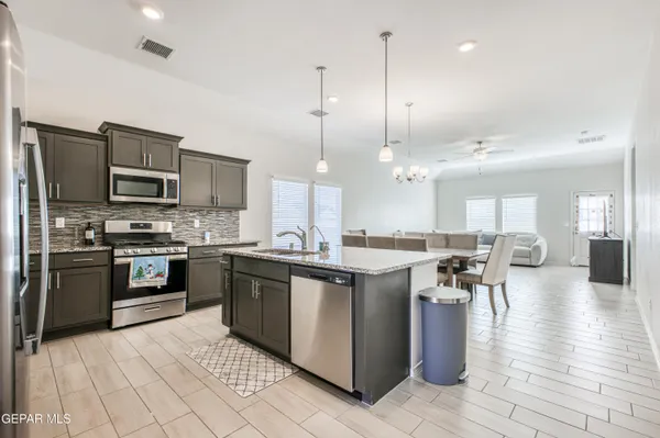 a kitchen with stainless steel appliances granite countertop a stove top oven a sink dishwasher a dining table and chairs with wooden floor