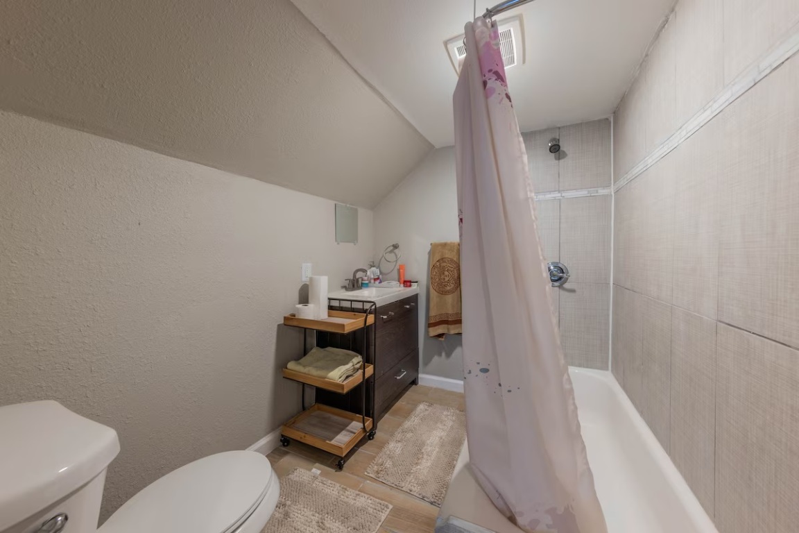 1212 North Main Street Elgin, TX 78621 - Photo 21 of 31 Bathroom with vaulted ceiling, a textured wall, vanity, shower / bathtub combination with curtain, and a textured ceiling