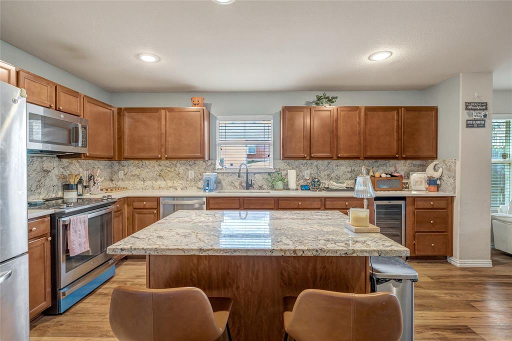 3216 Jetranger Road Fort Worth, TX 76053 - Photo 11 of 35 Kitchen with light wood-style flooring, brown cabinetry, stainless steel appliances, a center island, and a breakfast bar area