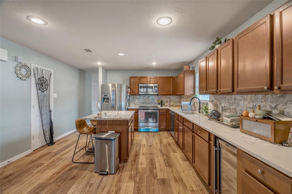 3216 Jetranger Road Fort Worth, TX 76053 - Photo 14 of 35 Kitchen featuring brown cabinetry, appliances with stainless steel finishes, a kitchen bar, a center island, and tasteful backsplash