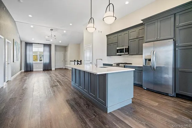 a large kitchen with stainless steel appliances a large counter top a sink a refrigerator and a window