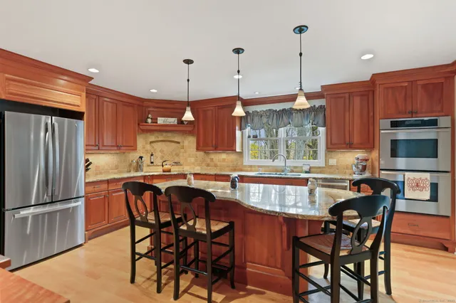 a kitchen with stainless steel appliances granite countertop a stove a refrigerator a kitchen island a dining table and chairs with wooden floor