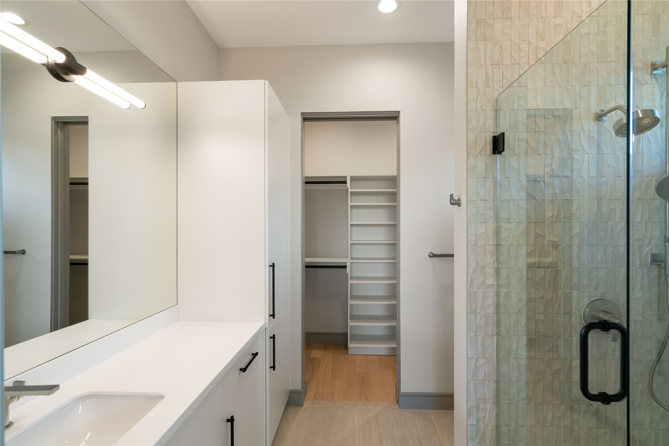 47 Pronghorn Place Spring, TX 77389 - Photo 32 of 44 This modern bathroom features a sleek design with a large mirror, a white vanity with ample storage, a glass-enclosed shower, and an adjoining walk-in closet with built-in shelving.