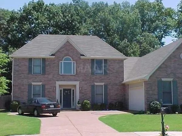 a brick house with a small yard plants and a large tree