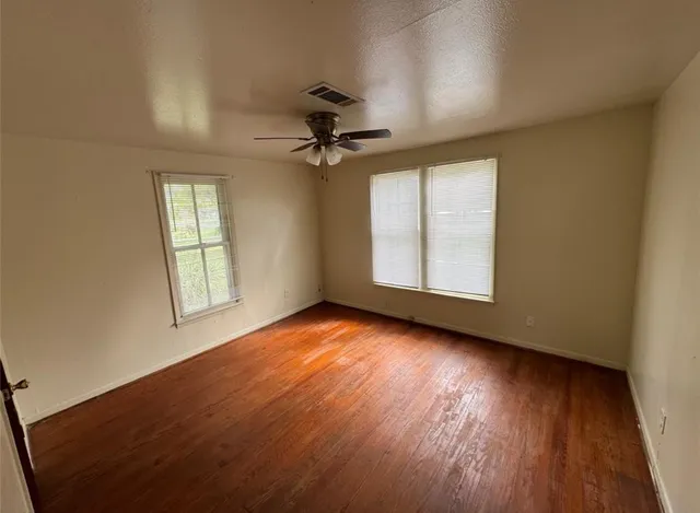 an empty room with wooden floor chandelier fan and windows
