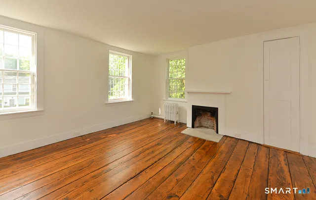 an empty room with wooden floor fireplace and windows