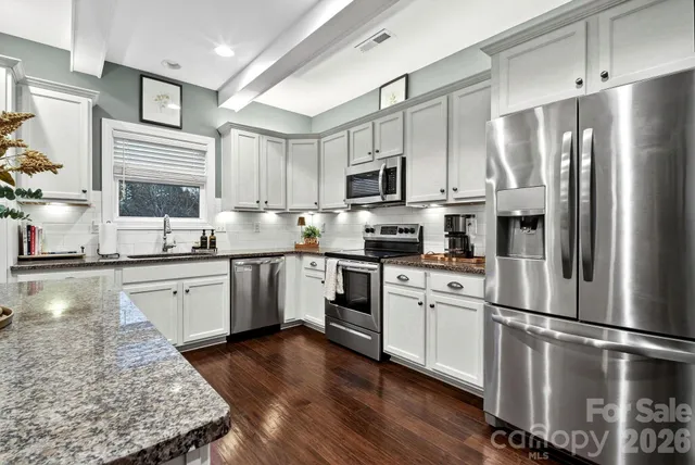 a kitchen with stainless steel appliances granite countertop a refrigerator a stove a sink dishwasher a microwave oven with white cabinets and wooden floor