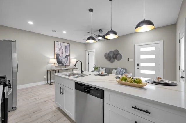 a kitchen with stainless steel appliances a refrigerator a stove a sink dishwasher a dining table and chairs with wooden floor