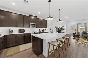 a kitchen with stainless steel appliances kitchen island granite countertop a sink a stove and chairs with wooden floor