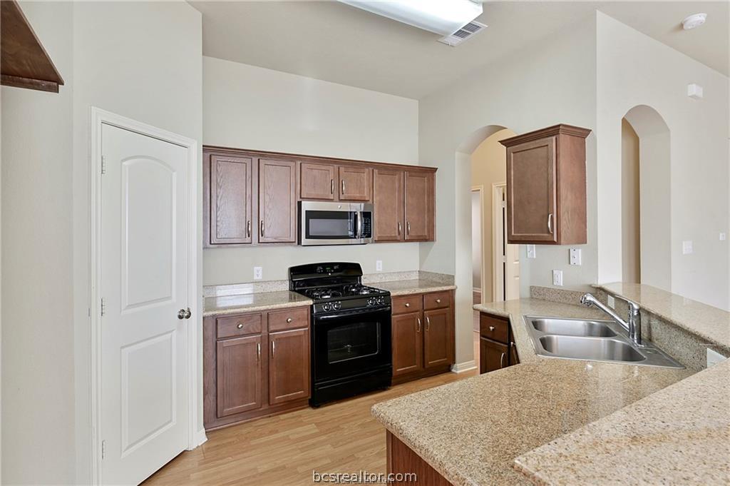 2004 Spring Leaf Court Bryan, TX 77807 - Photo 4 of 19 Kitchen featuring a sink, black gas range, a peninsula, stainless steel microwave, and light wood-style floors