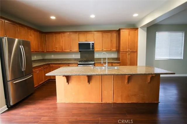 a kitchen with stainless steel appliances granite countertop a refrigerator a sink dishwasher a stove and a microwave oven on the wooden floor