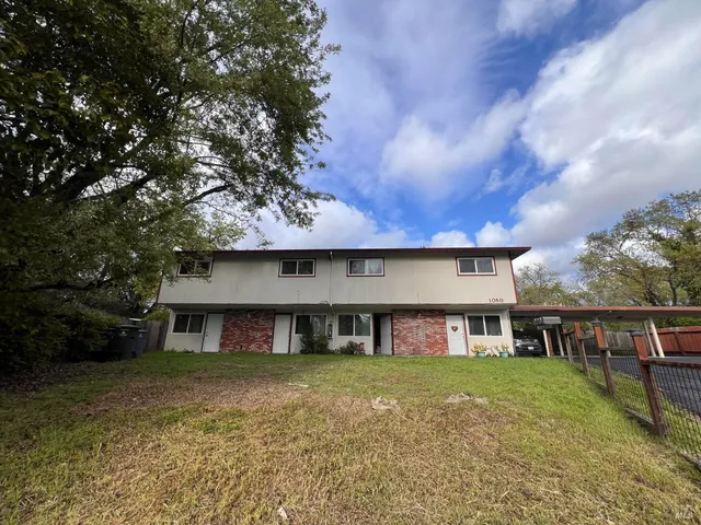 a view of a house with a yard plants and large tree
