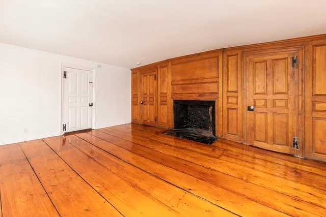 an empty room with wooden floor fireplace and windows