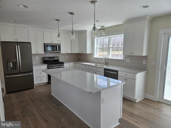 a kitchen with stainless steel appliances granite countertop a sink a stove a refrigerator a center island and wooden floor