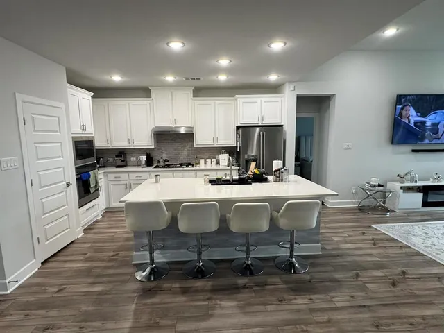 a kitchen with stainless steel appliances a dining table chairs refrigerator and sink