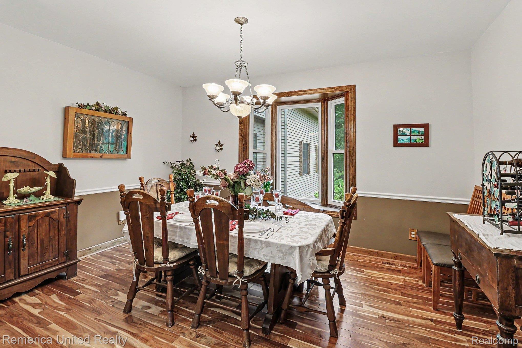 20962 Wasson Road Gregory, MI 48137 - Photo 6 of 39 Dining area featuring wood-finish flooring, a contemporary chandelier, a large window with wood trim, and a two-tone wall treatment with chair rail molding