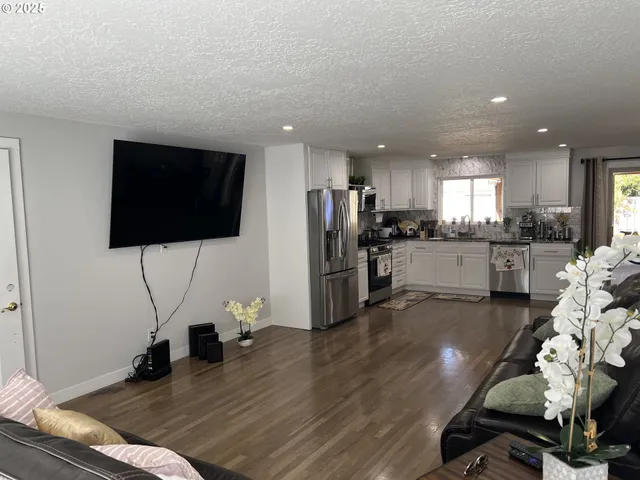 a kitchen with stainless steel appliances kitchen island granite countertop a refrigerator oven a sink a dining table and chairs with wooden floor