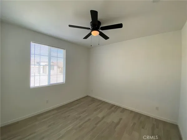 an empty room with wooden floor ceiling fan and window