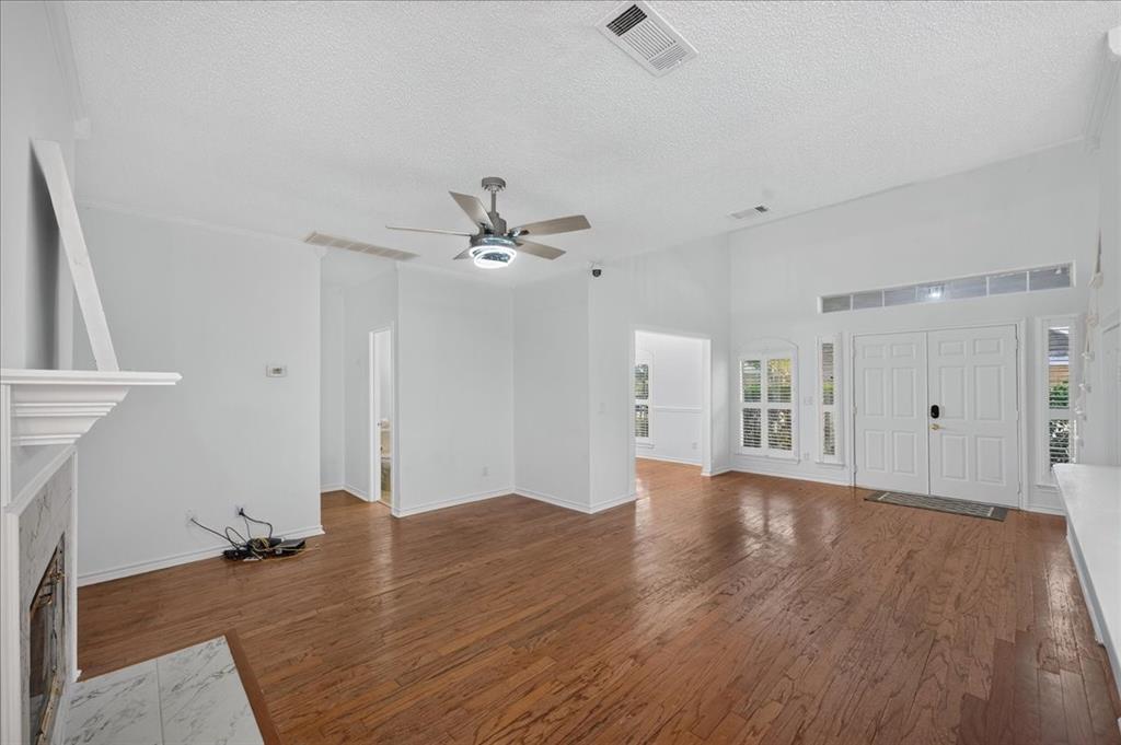 Vaulted ceilings, wood-finish flooring, a fireplace with a stone surround and mantel, a ceiling fan with integrated lighting, and a double-door entry with transom windows