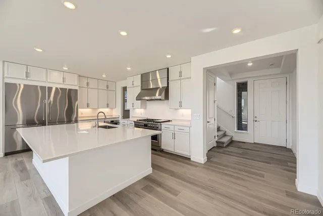 a kitchen with stainless steel appliances a refrigerator oven a sink a stove and white cabinets with wooden floor