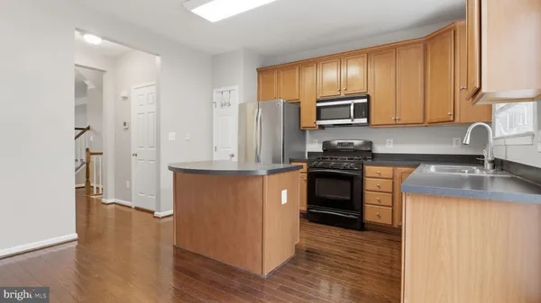 a kitchen with granite countertop wooden cabinets a sink a stove a refrigerator and island with wooden floor