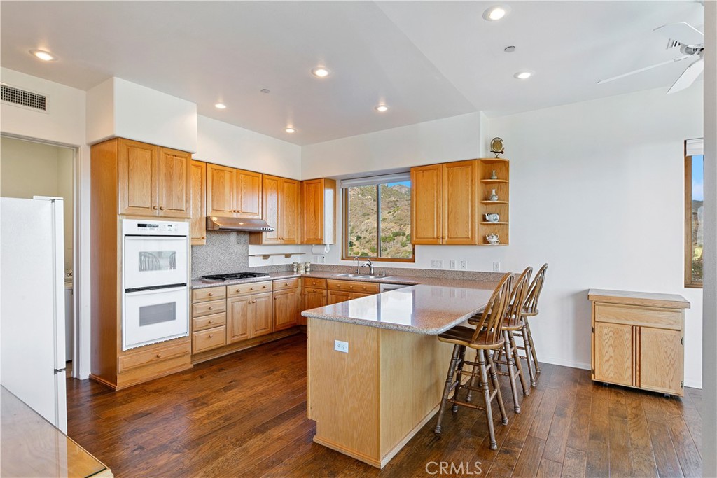 8400 Mipolomol Road Malibu, CA 90265 - Photo 16 of 58 a kitchen with stainless steel appliances granite countertop a refrigerator a stove top oven a sink dishwasher and white cabinets with wooden floor