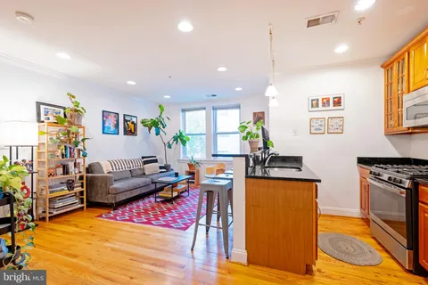 a kitchen with stainless steel appliances granite countertop a refrigerator a stove top oven a dining table and chairs with wooden floor